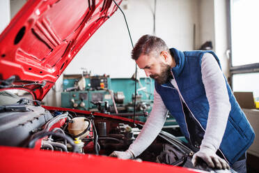 Älterer Mann, der ein Auto in einer Garage repariert. - HPIF27336