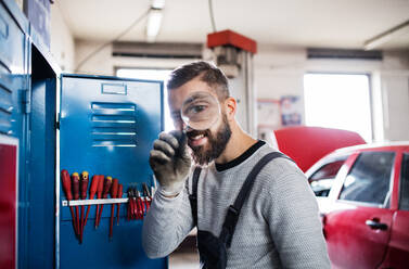 Portrait of a man mechanic standing in a garage, using a magnifying glass. - HPIF27339