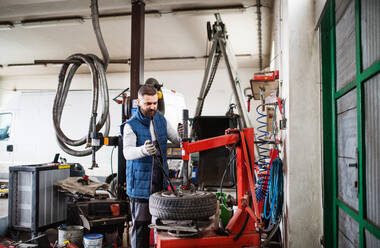 Mature man mechanic repairing a car in a garage. - HPIF27342