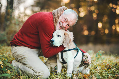 Ein glücklicher älterer Mann mit einem Hund bei einem Spaziergang in der herbstlichen Natur bei Sonnenuntergang. - HPIF27363