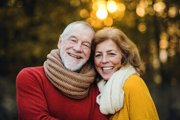 Ein fröhliches, verliebtes älteres Paar steht in einer herbstlichen Natur bei Sonnenuntergang und umarmt sich. - HPIF27379