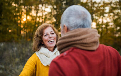 Ein fröhliches, verliebtes älteres Paar, das in der herbstlichen Natur bei Sonnenuntergang steht und sich gegenseitig anschaut. - HPIF27383