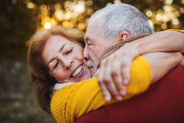 Ein fröhliches, verliebtes älteres Paar in herbstlicher Natur bei Sonnenuntergang, das sich umarmt und küsst. - HPIF27384