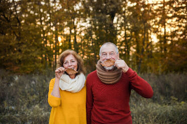 A cheerful senior couple in love standing in an autumn nature at sunset, having fun. - HPIF27389