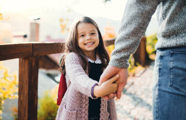 A small girl holding a hand of an unrecognizable father on a walk in sunny autumn. - HPIF27400