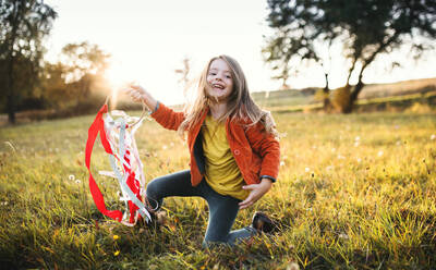 A happy small girl playing with a rainbow hand kite in autumn nature at sunset. - HPIF27405