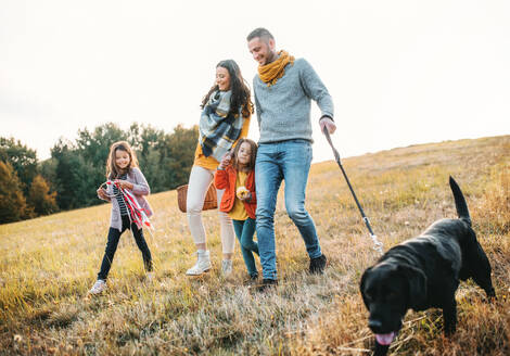 Eine junge Familie mit zwei kleinen Kindern und einem schwarzen Hund bei einem Spaziergang in der herbstlichen Natur. - HPIF27407