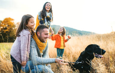 Eine junge Familie mit zwei kleinen Kindern und einem schwarzen Hund bei einem Spaziergang in der herbstlichen Natur. - HPIF27408