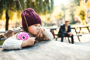Ein Porträt von einem gelangweilten kleinen Kleinkind Mädchen sitzen im Park im Herbst Natur. - HPIF27409