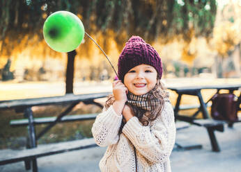 A portrait of a small toddler girl holding balloon in park in sunny autumn nature. - HPIF27410