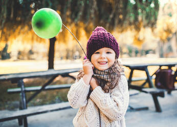 Ein Porträt eines kleinen Kleinkindes Mädchen hält Ballon im Park in sonnigen Herbst Natur. - HPIF27410