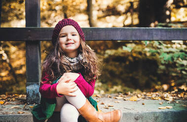 A portrait of a small toddler girl sitting with crossed legs in forest in autumn nature. - HPIF27416