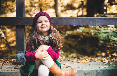 Ein Porträt eines kleinen Kleinkindes Mädchen sitzt mit gekreuzten Beinen im Wald im Herbst Natur. - HPIF27416