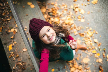 Porträt eines kleinen Mädchens, das in einem Park in der herbstlichen Natur sitzt und nach oben schaut, Ansicht von oben. - HPIF27417