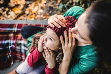 Eine unerkennbare junge Mutter mit einer kleinen Tochter sitzt im Wald in herbstlicher Natur. - HPIF27453