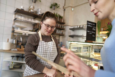 Lächelnder Café-Besitzer mit Down-Syndrom hilft Kunden bei der Auswahl von Speisen aus der Speisekarte - ABIF01997