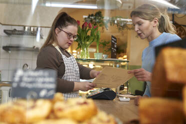 Café-Besitzer mit Down-Syndrom hilft Kunden bei der Bestellung von Speisen aus der Speisekarte im Café - ABIF02004