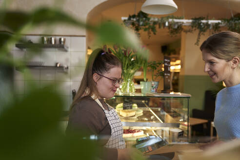 Lächelnder Café-Besitzer mit Down-Syndrom im Gespräch mit einem Kunden im Coffeeshop - ABIF02005