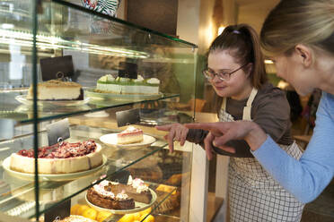 Café-Besitzer mit Down-Syndrom berät Kunden bei der Auswahl von Kuchen im Café - ABIF02013