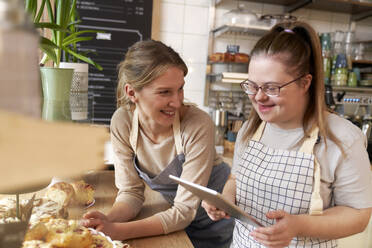 Happy coffee shop owner with down syndrome having discussion and checking commodities in cafe - ABIF02022