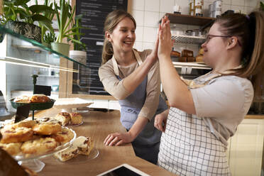 Happy coffee shop owner with down syndrome giving high-five in cafe - ABIF02023