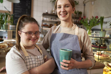 Happy coffee shop owner with down syndrome standing by colleague in cafe - ABIF02027