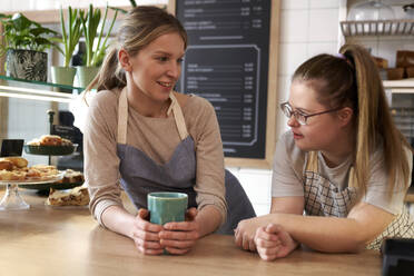 Smiling cafe owner with down syndrome talking to colleague - ABIF02028