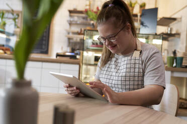 Lächelnder Café-Besitzer mit Down-Syndrom benutzt Tablet-PC am Tisch im Café - ABIF02033
