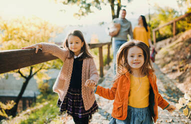 Two girls with unrecognizable parents in the background walking in park in autumn, holding hands. - HPIF27465