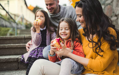 Porträt einer jungen Familie mit zwei kleinen Kindern in der Stadt im Herbst, die Äpfel essen. - HPIF27477