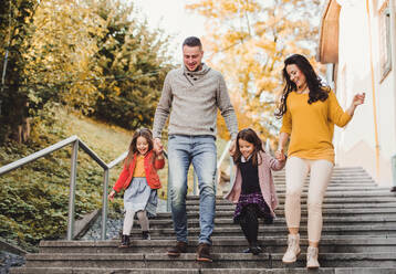 Eine glückliche junge Familie mit Kindern, die im Herbst draußen in der Stadt die Treppe hinuntergeht. - HPIF27479