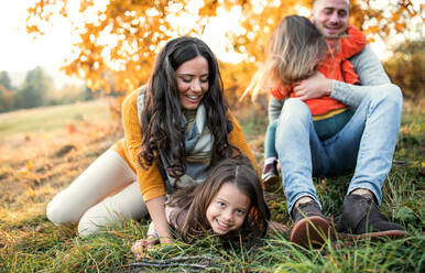 A portrait of happy young family with two small children sitting on a ground in autumn nature at sunset. - HPIF27483