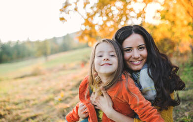 Ein Porträt einer jungen Mutter mit einer kleinen Tochter, die in der herbstlichen Natur bei Sonnenuntergang sitzt. - HPIF27484