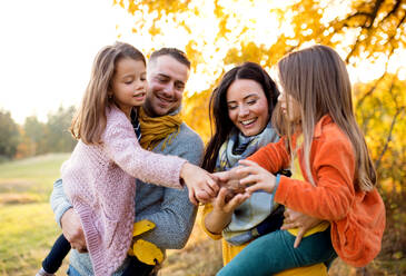 Ein Porträt einer glücklichen jungen Familie mit zwei kleinen Kindern, die Nüsse in der herbstlichen Natur halten. - HPIF27490