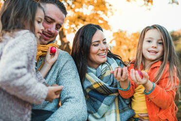 Ein Porträt einer glücklichen jungen Familie mit zwei kleinen Kindern, die Nüsse und Äpfel in der herbstlichen Natur halten. - HPIF27491