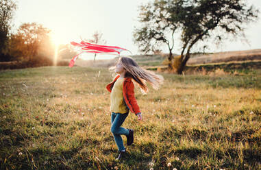 A happy small girl playing with a rainbow hand kite in autumn nature at sunset. - HPIF27499