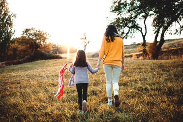 Rückansicht einer jungen Mutter mit einer kleinen Tochter, die in der herbstlichen Natur bei Sonnenuntergang spazieren geht. - HPIF27504