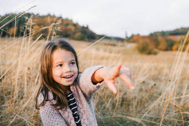 Ein glückliches kleines Mädchen, das in der herbstlichen Natur steht und mit dem Finger auf etwas zeigt. Raum kopieren. - HPIF27506
