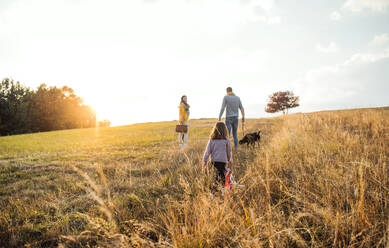 Rückansicht einer Familie mit Kind und Hund bei einem Spaziergang in der herbstlichen Natur bei Sonnenuntergang. Raum kopieren. - HPIF27507