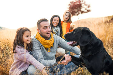 Eine junge Familie mit zwei kleinen Kindern und einem schwarzen Hund auf einer Wiese in herbstlicher Natur. - HPIF27514