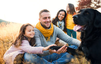 Eine junge Familie mit zwei kleinen Kindern und einem schwarzen Hund auf einer Wiese in herbstlicher Natur. - HPIF27517