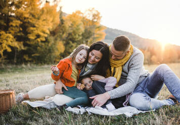 Ein Porträt von glücklichen jungen Familie mit zwei kleinen Kindern sitzen auf einem Boden im Herbst Natur bei Sonnenuntergang. - HPIF27530