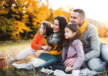 Ein Porträt von glücklichen jungen Familie mit zwei kleinen Kindern sitzen auf einem Boden im Herbst Natur bei Sonnenuntergang. - HPIF27531