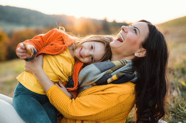 A portrait of young mother with a small daughter sitting on a ground in autumn nature at sunset. - HPIF27533