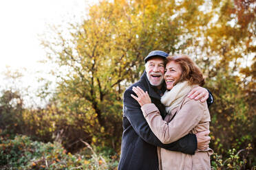 Aktives älteres Paar auf einem Spaziergang in der schönen Herbstnatur. Ein Mann und eine Frau stehen und umarmen sich. Platz kopieren. - HPIF27545
