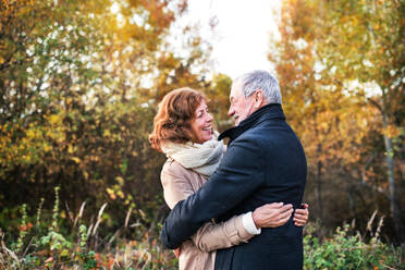 Aktives Seniorenpaar bei einem Spaziergang in der schönen Herbstnatur. Ein Mann und eine Frau schauen sich an und umarmen sich. - HPIF27546