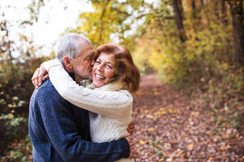 Ein aktives Seniorenpaar auf einem Spaziergang in der schönen Herbstnatur. Ein Mann und eine Frau, die sich umarmen und küssen. Kopierraum. - HPIF27565