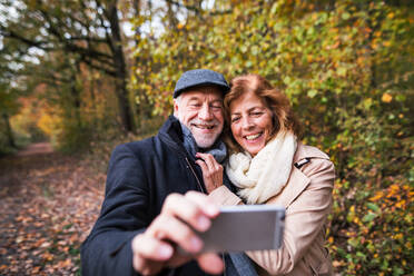 Ein glückliches älteres Paar genießt einen romantischen Spaziergang inmitten einer atemberaubenden Herbstlandschaft und hält die Erinnerungen mit einem Selfie fest - HPIF27571