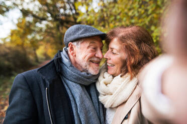 Ein glückliches älteres Paar genießt einen romantischen Spaziergang inmitten einer atemberaubenden Herbstlandschaft und hält die Erinnerungen mit einem Selfie fest - HPIF27572