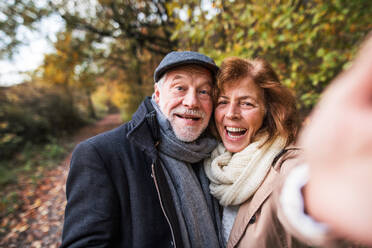 Ein glückliches älteres Paar genießt einen romantischen Spaziergang inmitten einer atemberaubenden Herbstlandschaft und hält die Erinnerungen mit einem Selfie fest - HPIF27573